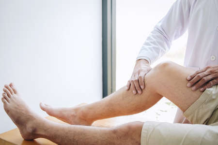 Doctor physiotherapist assisting a male patient while giving exercising treatment massaging the leg...
