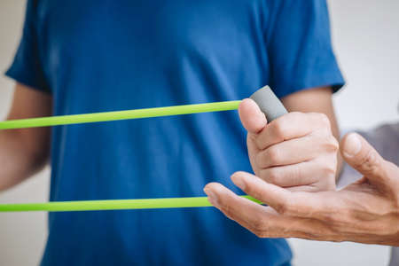 Doctor physiotherapist assisting a male patient while giving exercising treatment on stretching his...