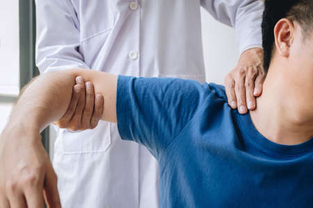 Doctor physiotherapist assisting a male patient while giving exercising treatment massaging the shoulder of patient in a physio room, rehabilitation physiotherapy concept.の写真素材