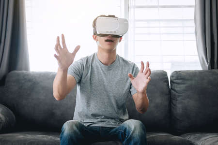 Young asian man having fun wearing playing virtual reality headset glasses to enjoying in holiday at...