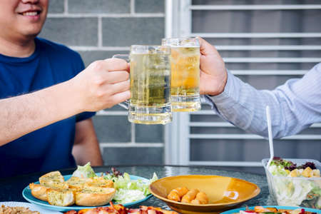 Two young man hand raise a glass of beer to celebrate the holiday festival happy drinking beer outdoors and enjoying at home.の写真素材