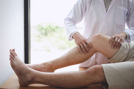 Doctor physiotherapist assisting a male patient while giving exercising treatment massaging the leg of patient in a physio room, rehabilitation physiotherapy concept.の写真素材