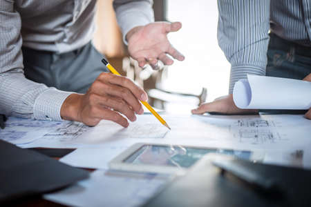 Construction engineering or architect discuss a blueprint while checking information on drawing and...