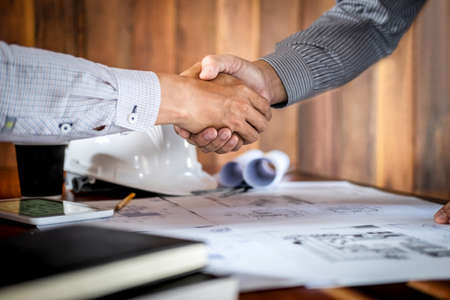 Handshake of collaboration, Construction engineering or architect discuss a blueprint and building model while checking information on sketching, meeting for architectural project of partner.の写真素材