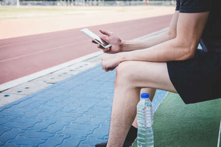 Young fitness athlete man resting on bench with bottle of water preparing to running on road track, exercise workout wellness concept.の写真素材