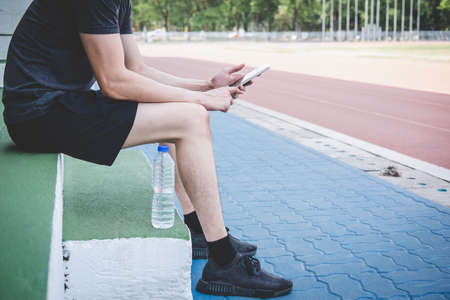Young fitness athlete man resting on bench with bottle of water preparing to running on road track,...