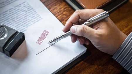 Close up hands of businessman signing and stamp on paper document to approve business investment contract agreement.の写真素材