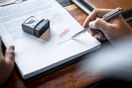 Close up hands of businessman signing and stamp on paper document to approve business investment contract agreement.の写真素材