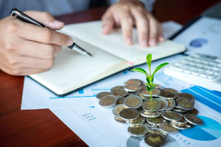 Businessman accountant making notes at report doing finances and calculate about cost of investment and analyzing financial data, growing business to profit and saving with wealth management.の写真素材