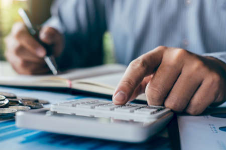 Businessman accountant making notes at report doing finances and calculate about cost of investment and analyzing financial data, growing business to profit and saving with wealth management.の写真素材