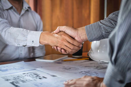 Handshake of collaboration, Construction engineering or architect discuss a blueprint and building model while checking information on sketching, meeting for architectural project of partner.の写真素材