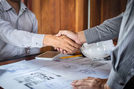 Handshake of collaboration, Construction engineering or architect discuss a blueprint and building model while checking information on sketching, meeting for architectural project of partner.の写真素材
