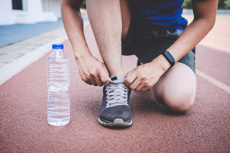 Young fitness athlete man running on road track, exercise workout wellness and runner tying shoelaces with copy space before run.の写真素材