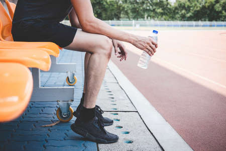 Young fitness athlete man resting on bench with bottle of water preparing to running on road track, exercise workout wellness concept.の写真素材