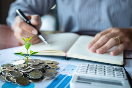 Businessman accountant making notes at report doing finances and calculate about cost of investment and analyzing financial data, growing business to profit and saving with wealth management.の写真素材