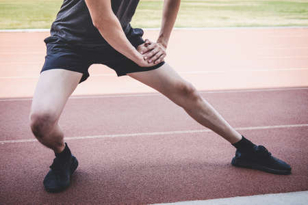 Young fitness athlete man running on road track, exercise workout wellness and runner stretching legs before run concept.の写真素材
