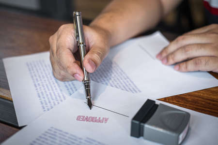 Close up hands of businessman signing and stamp on paper document to approve business investment contract agreement.の写真素材