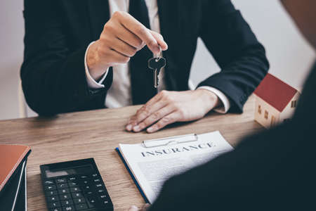 Estate agent giving house keys to client after signing agreement contract real estate with approved mortgage application form, concerning mortgage loan offer for and house insurance.の写真素材