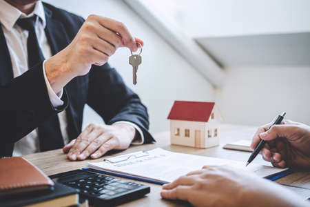 Estate agent giving house keys to client after signing agreement contract real estate with approved mortgage application form, concerning mortgage loan offer for and house insurance.の写真素材