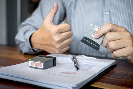 Hands of businessman stamp on paper document to approve business investment contract agreement.の写真素材