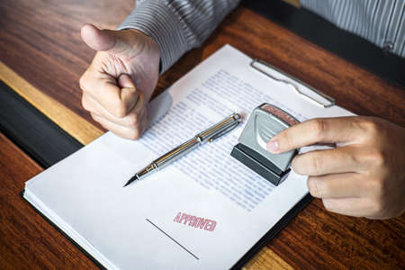 Hands of businessman stamp on paper document to approve business investment contract agreement.の写真素材