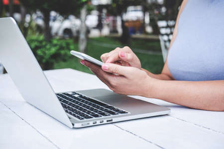 Young professional woman in smart casual wear working using laptop in outdoor workplace, holding...