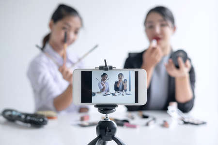 Business online on social media, Two Beautiful Woman Blogger is showing present tutorial beauty cosmetic product and broadcast live streaming video to social network while recording teaching online.の写真素材