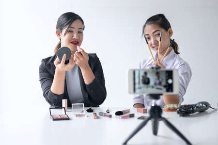 Business online on social media, Two Beautiful Woman Blogger is showing present tutorial beauty cosmetic product and broadcast live streaming video to social network while recording teaching online.の写真素材