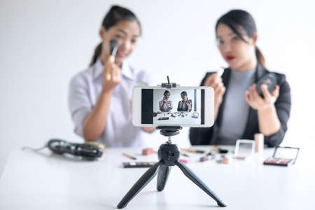 Business online on social media, Two Beautiful Woman Blogger is showing present tutorial beauty cosmetic product and broadcast live streaming video to social network while recording teaching online.の写真素材