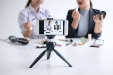 Business online on social media, Two Beautiful Woman Blogger is showing present tutorial beauty cosmetic product and broadcast live streaming video to social network while recording teaching online.の写真素材