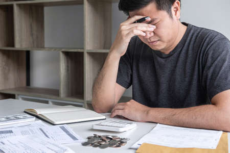 Images of stressed Husband using calculator to calculating expenditure receipt bills of various activity cost and expenses in home office and written make report to plan of spent.の写真素材