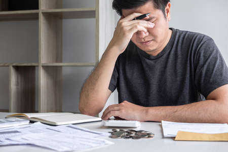 Images of stressed Husband using calculator to calculating expenditure receipt bills of various activity cost and expenses in home office and written make report to plan of spent.の写真素材