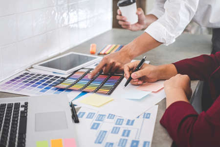 Teamwork of young creative designers working on project together and choose color samples for selection coloring on digital graphic tablet and equipment at workplace.の写真素材