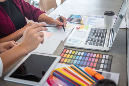 Teamwork of young creative designers working on project together and choose color swatch samples for selection coloring on digital graphic tablet and equipment at workplace.の写真素材