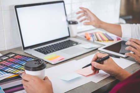 Teamwork of creative designers working on new project and choose color swatch samples for selection coloring on digital graphic tablet with work tools and equipment at workplace.の写真素材