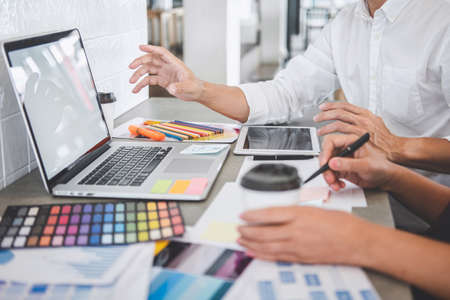 Teamwork of young creative designers working on project together and choose color swatch samples for selection coloring on digital graphic tablet and equipment at workplace.の写真素材