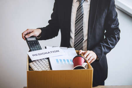 Businessman prepared will being sending resignation letter to company and carrying packing belongings and files into brown cardboard box, changing and resigning from work concept.の写真素材