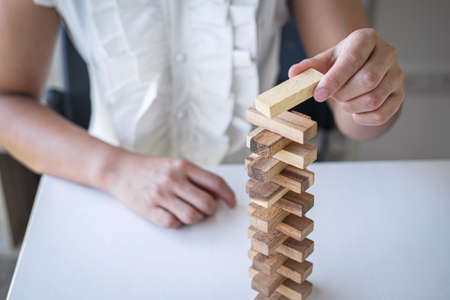 Alternative Risk and Strategy in Business, Hand of intelligent business woman gambling placing making wooden block hierarchy on the tower to planning and development to successful.の写真素材