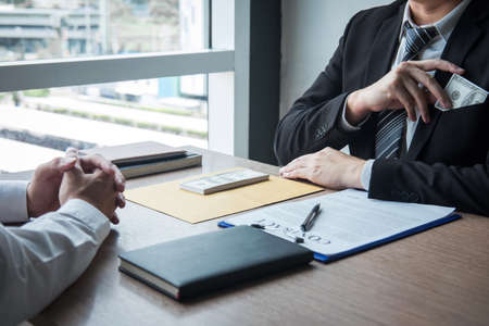 Dishonest cheating in illegal money, Businessman giving bribe money the form of dollar bills to while give success the deal to contract agreement, Bribery and corruption concept.の写真素材