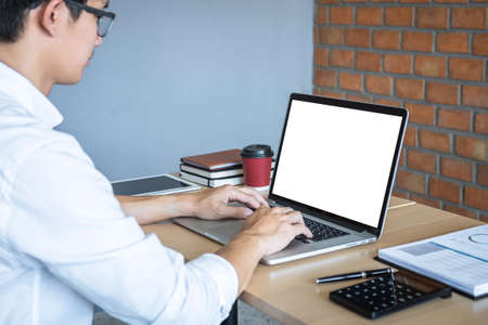 Image of Young man working in front of the laptop looking at screen with a clean white screen and blank space for text and hand typing information on keyboard in modern workspace.の写真素材
