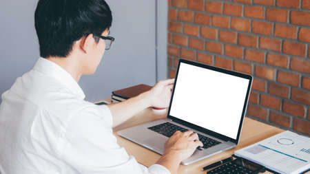 Image of Young man working in front of the laptop looking at screen with a clean white screen and blank space for text and hand typing information on keyboard in modern workspace.の写真素材