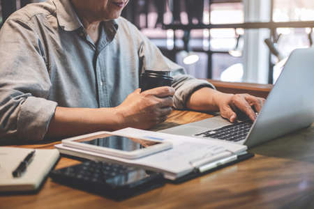Senior professional man in casual wear working using laptop in cafe, holding a cup of coffee, business working connecting to wireless via computer.の写真素材