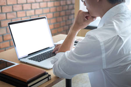 Image of Young man working in front of the laptop looking at screen with a clean white screen and blank space for text and hand typing information on keyboard in modern workspace.の写真素材