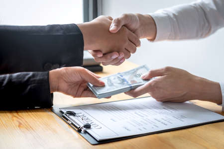 Dishonest cheating in business illegal money, Businessman handshake with money of dollar banknotes in hands from while give success the deal, Bribery and corruption concept.の写真素材