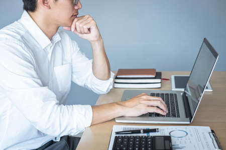 Image of Young man working in front of the laptop looking at screen with a clean white screen and blank space for text and hand typing information on keyboard in modern workspace.の写真素材
