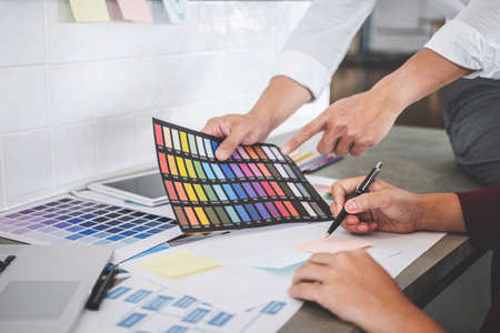 Teamwork of creative designers working on new project and choose color swatch samples for selection coloring on digital graphic tablet with work tools and equipment at workplace.の写真素材