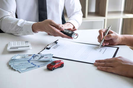 Car rent agent manager holding key of new car giving to woman client after signing good deal agreement contract, renting considering vehicle.の写真素材
