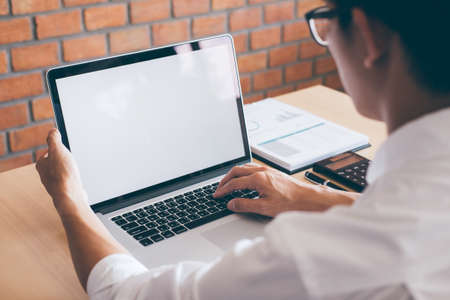 Image of Young man working in front of the laptop looking at screen with a clean white screen and blank space for text and hand typing information on keyboard in modern workspace.の写真素材
