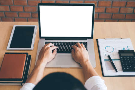 Image of Young man working in front of the laptop looking at screen with a clean white screen and blank space for text and hand typing information on keyboard in modern workspace.の写真素材