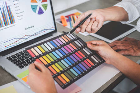 Teamwork of young creative designers working on project together and choose color swatch samples for selection coloring on digital graphic tablet and equipment at workplace.の写真素材